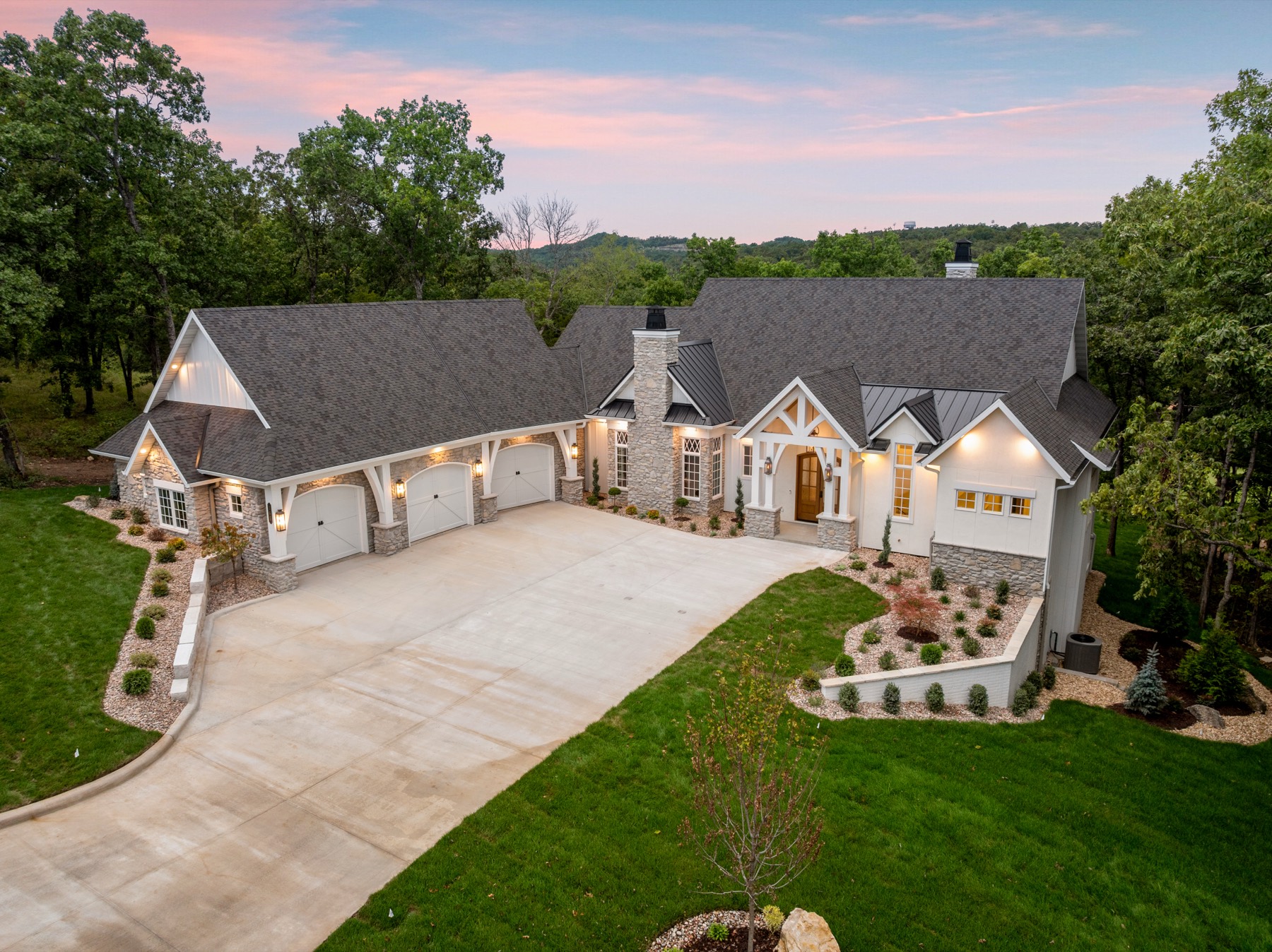 White craftsman home with stone chimney and three-car garage at dusk