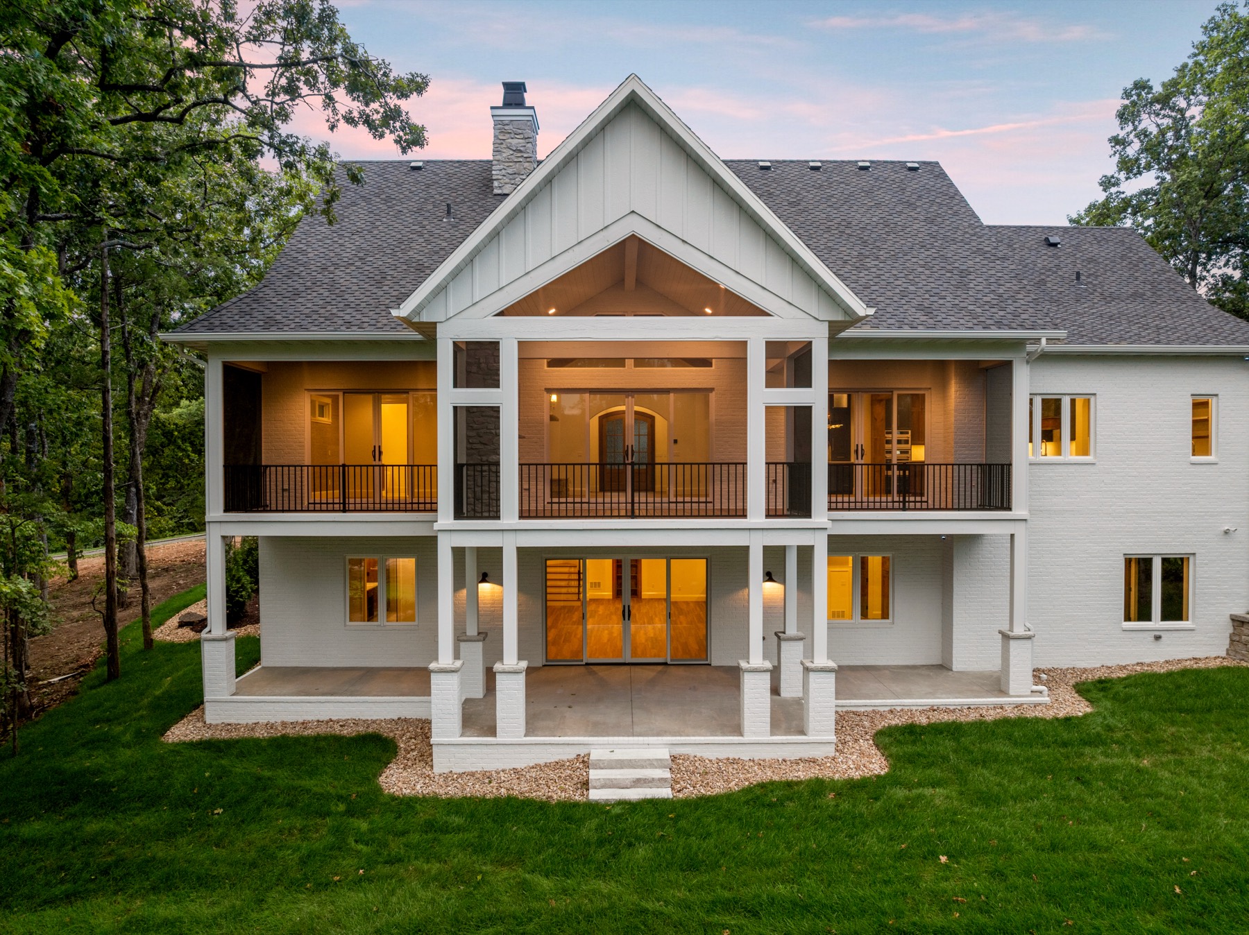 Back of a craftsman home at dusk with a lit two-story covered porch