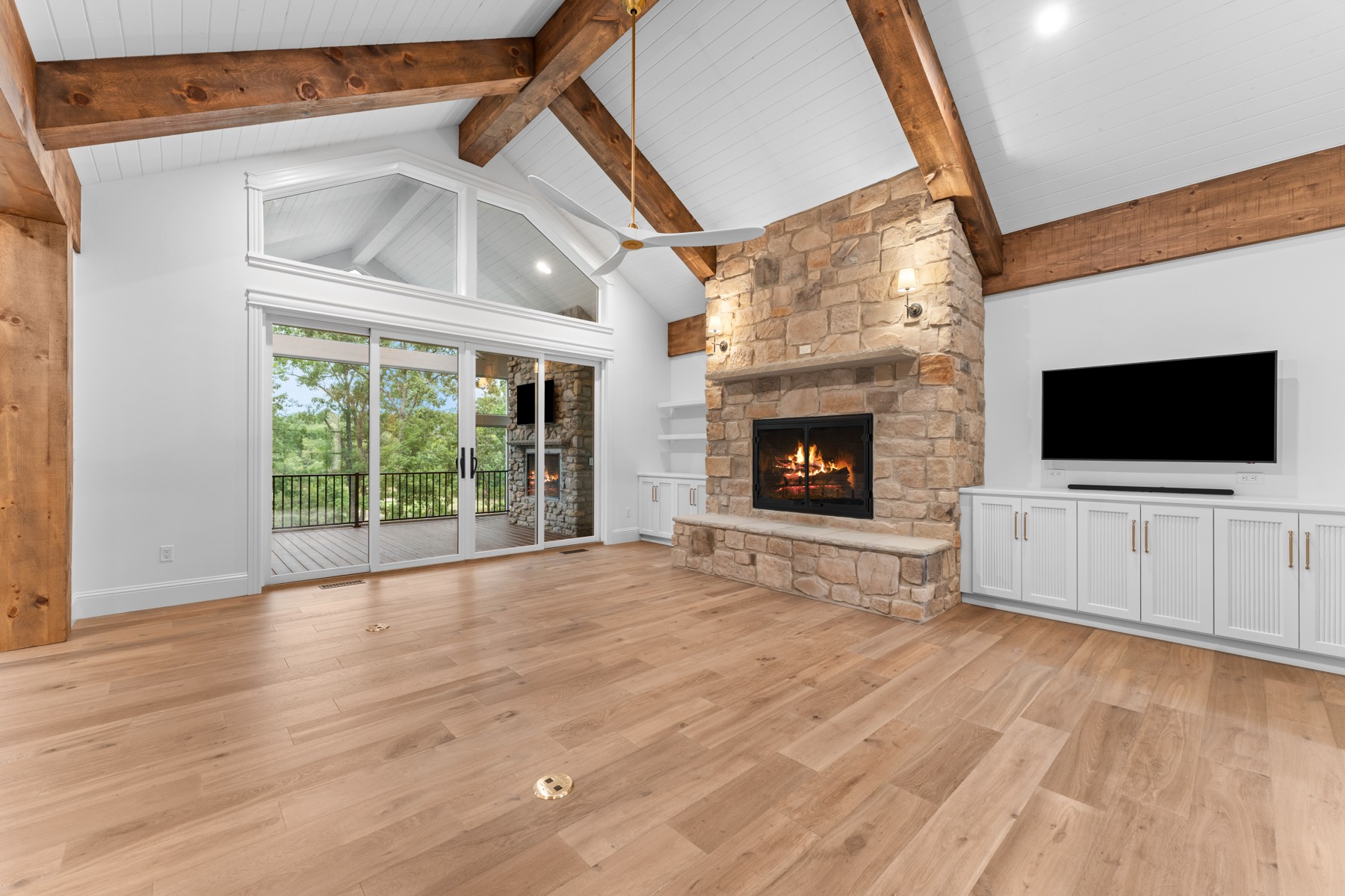 Great room with a stone fireplace, timber beams, and wide plank floors