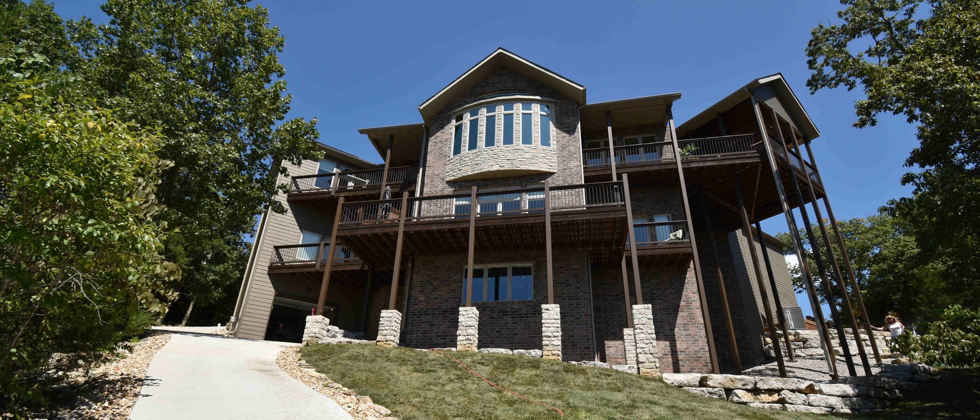 The lake side of a brick and stone home, three levels of decks rising above the lawn