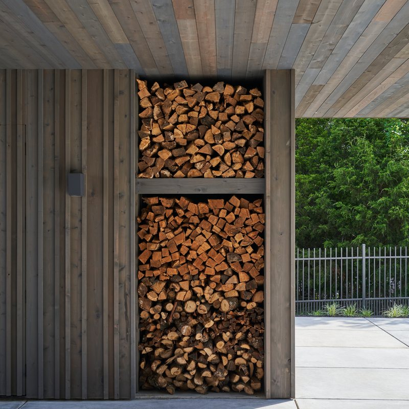 Cedar entry door beside a stacked firewood niche