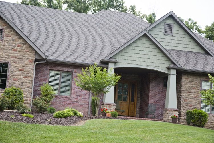 A brick and stone home with a green gable over the front entry