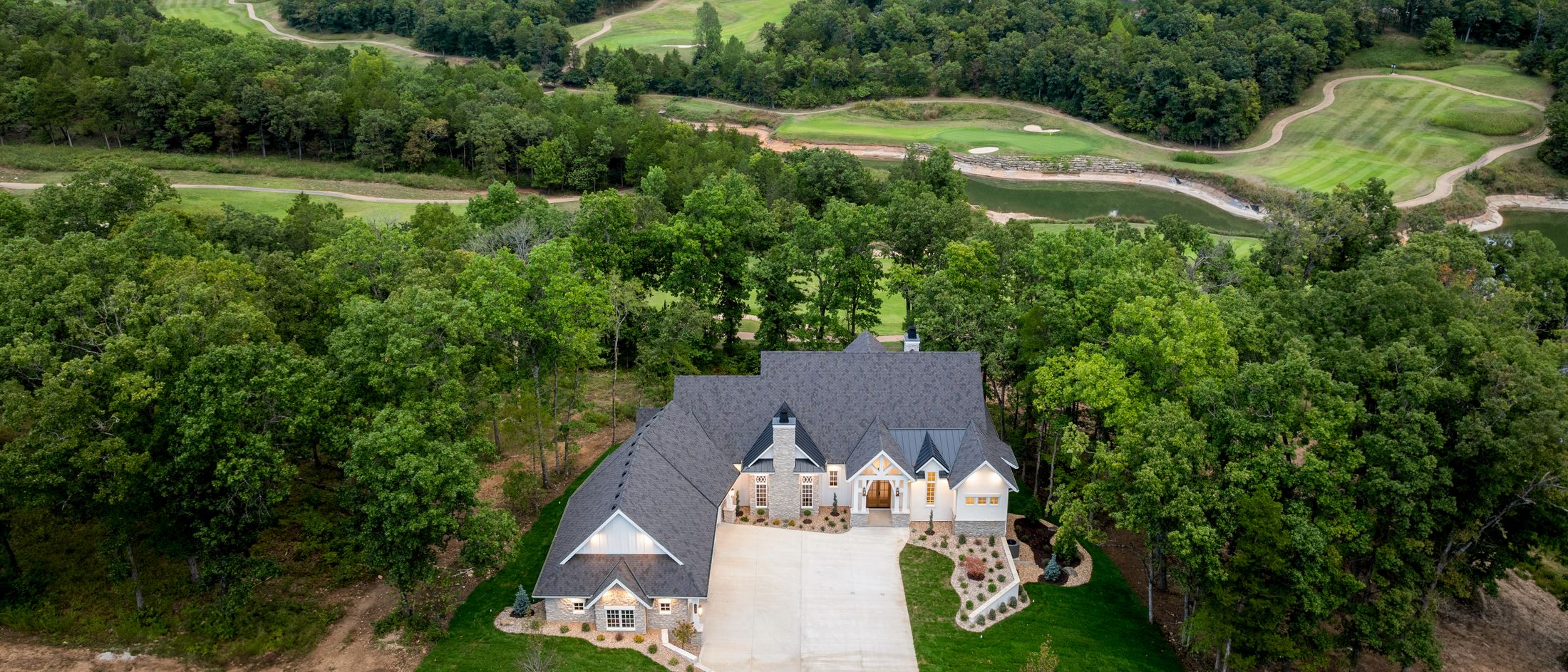A craftsman home seen from the air at dusk, set into the trees above the valley