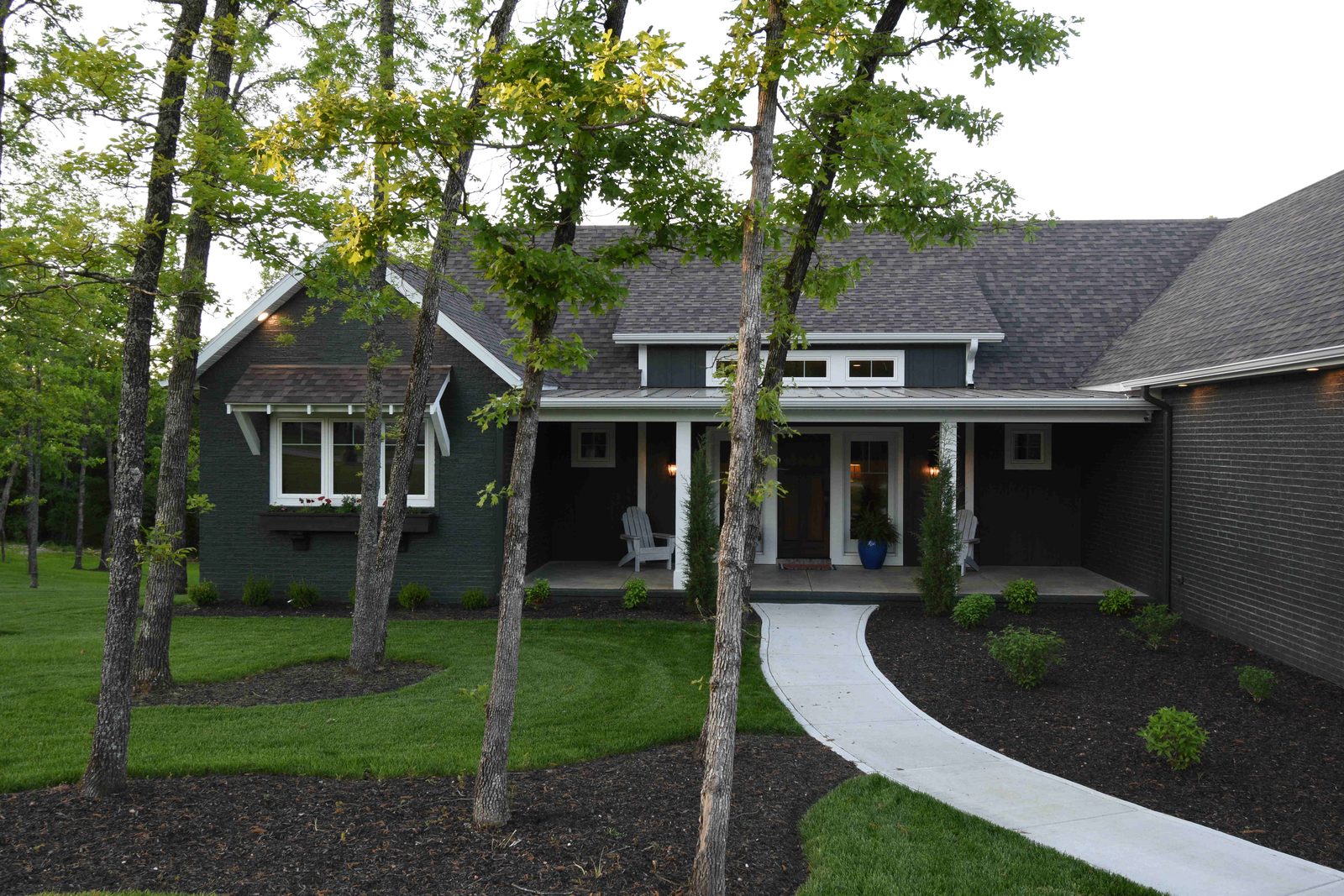 Dark board and batten craftsman home with deep covered porches under tall trees