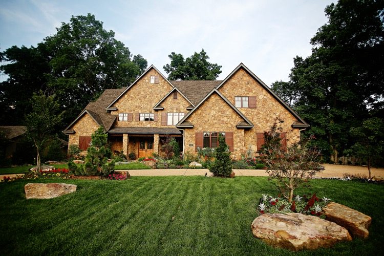 A brick and stone home with flower beds along the drive