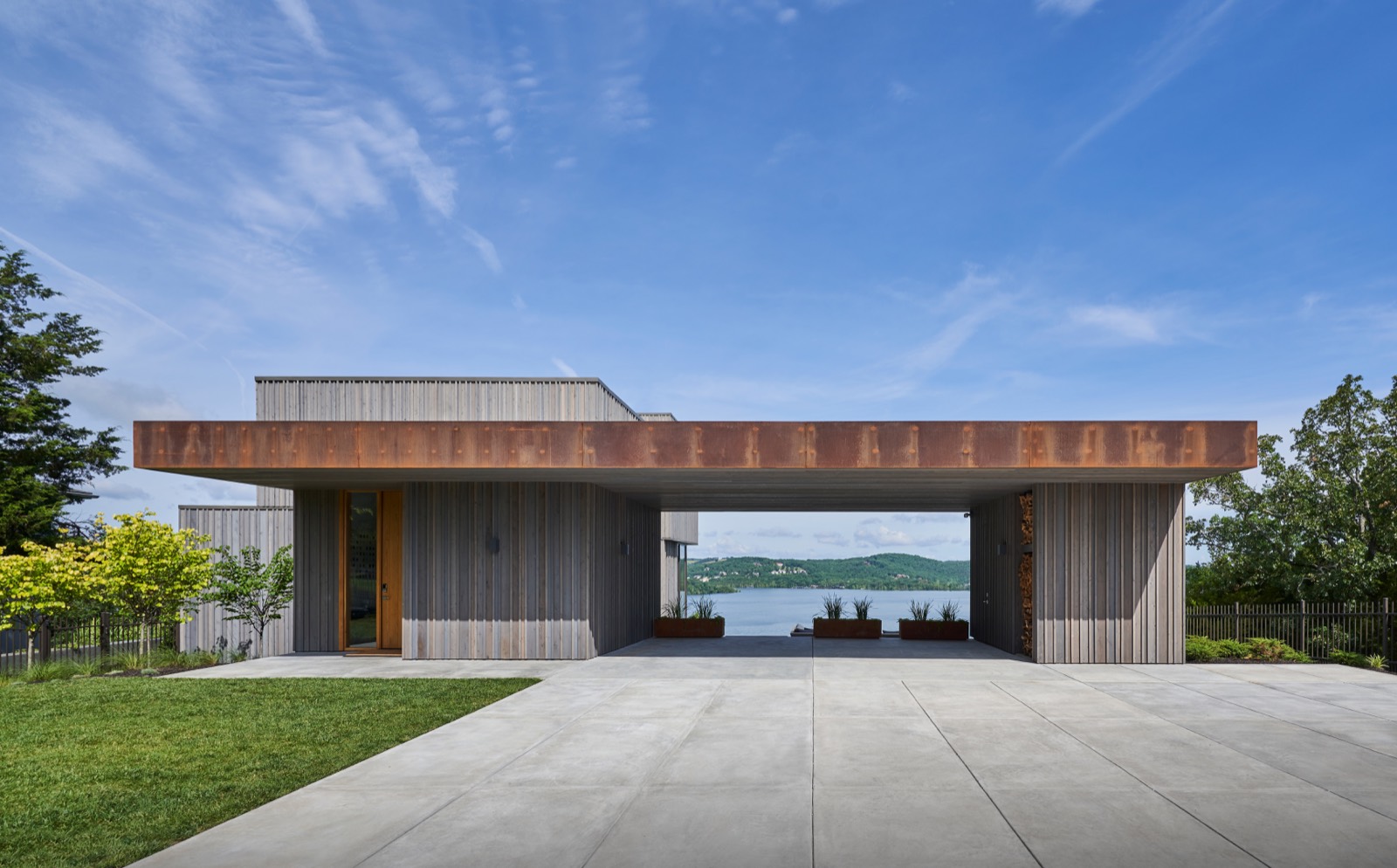 The low cedar house from the drive, with the breezeway open to the lake beyond