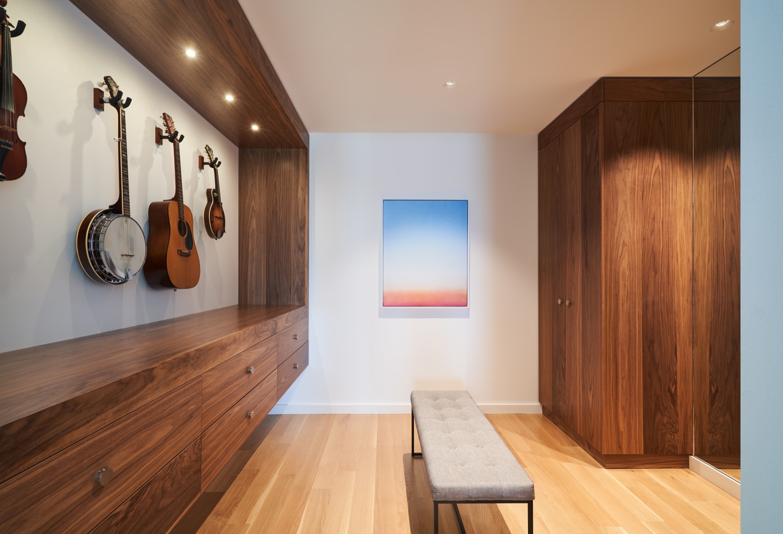 A wall of guitars above a white oak bench