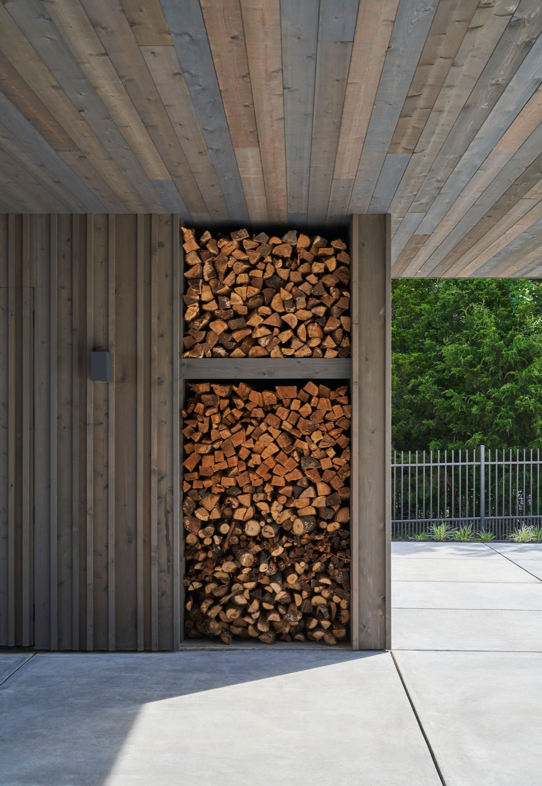 Cedar entry door beside a stacked firewood niche