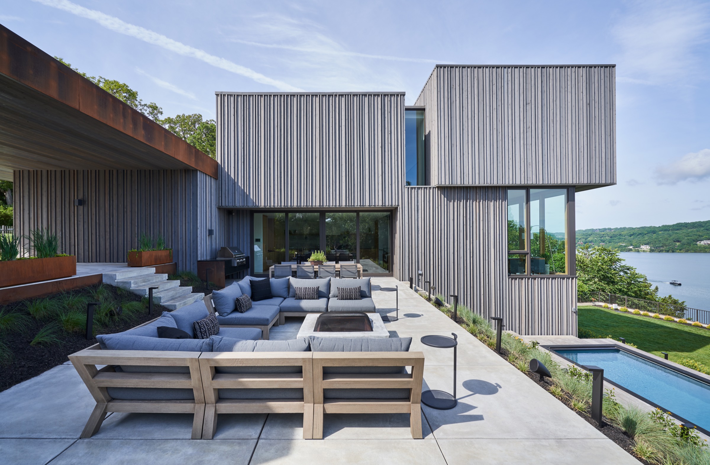 Terrace with outdoor seating, a fire table, and a lap pool beside a cedar lake home